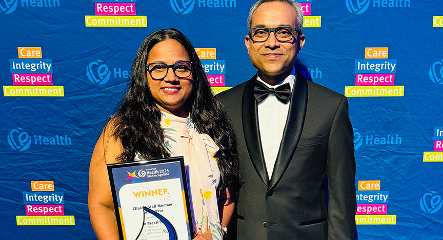Healthcare workers wearing cocktail attire stand in front of a royal blue media wall printed with Central Queensland Health values at an awards presentation evening at a conference centre.